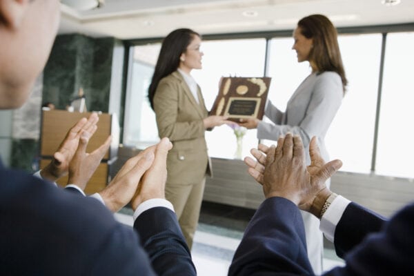 one woman hands another an award as people in the audience clap