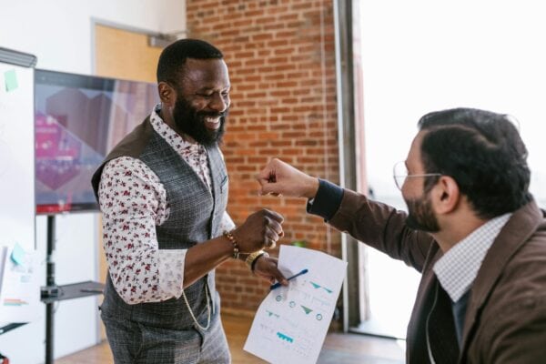 two men in business casual clothing fist bump each other
