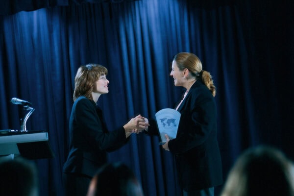 one woman handing another an award and shaking hands