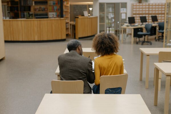 professor and student sitting next to each other in library photographed from behind