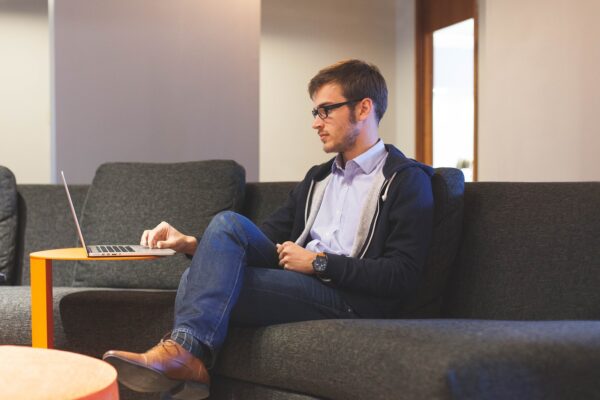 man sitting on couch with legs crossed scrolling on laptop