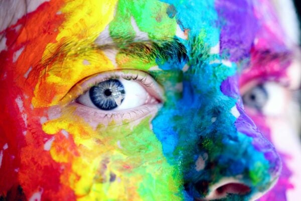 A face painted as the rainbow with blue eyes staring