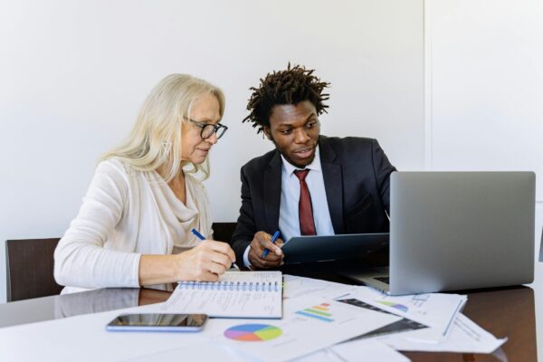 Two business people, taking notes and attending an online session by computer.
