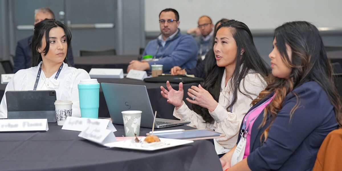 A group of diverse individuals seated at a table, each using a laptop for collaborative work and discussion.