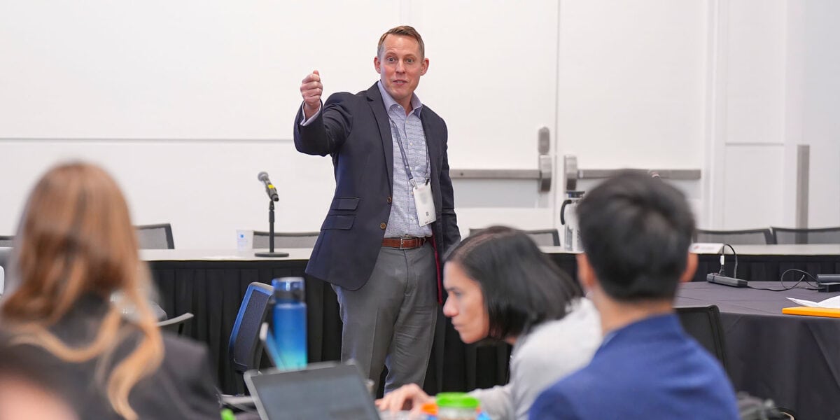 A man presenting to an audience, engaging with a group of attentive listeners in a conference setting.