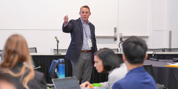 A man presenting to an audience, engaging with a group of attentive listeners in a conference setting.