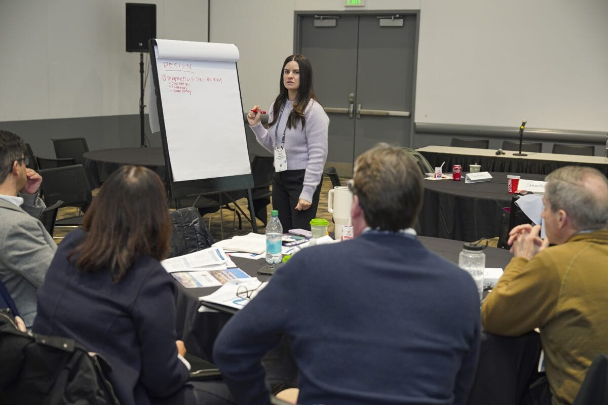 A woman stands before a group, delivering a presentation and interacting with her audience.