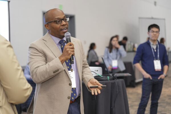 A man in a suit and tie delivers a speech into a microphone at a formal event.
