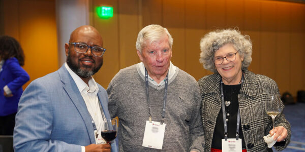 Three individuals stand together at an event, each holding a wine glass and posing for a picture.
