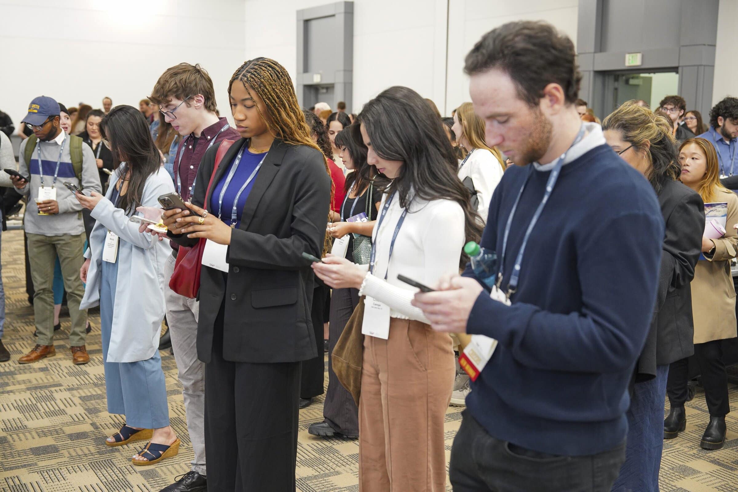 A group of people standing in a line, each focused on their phones, with varied expressions of concentration.