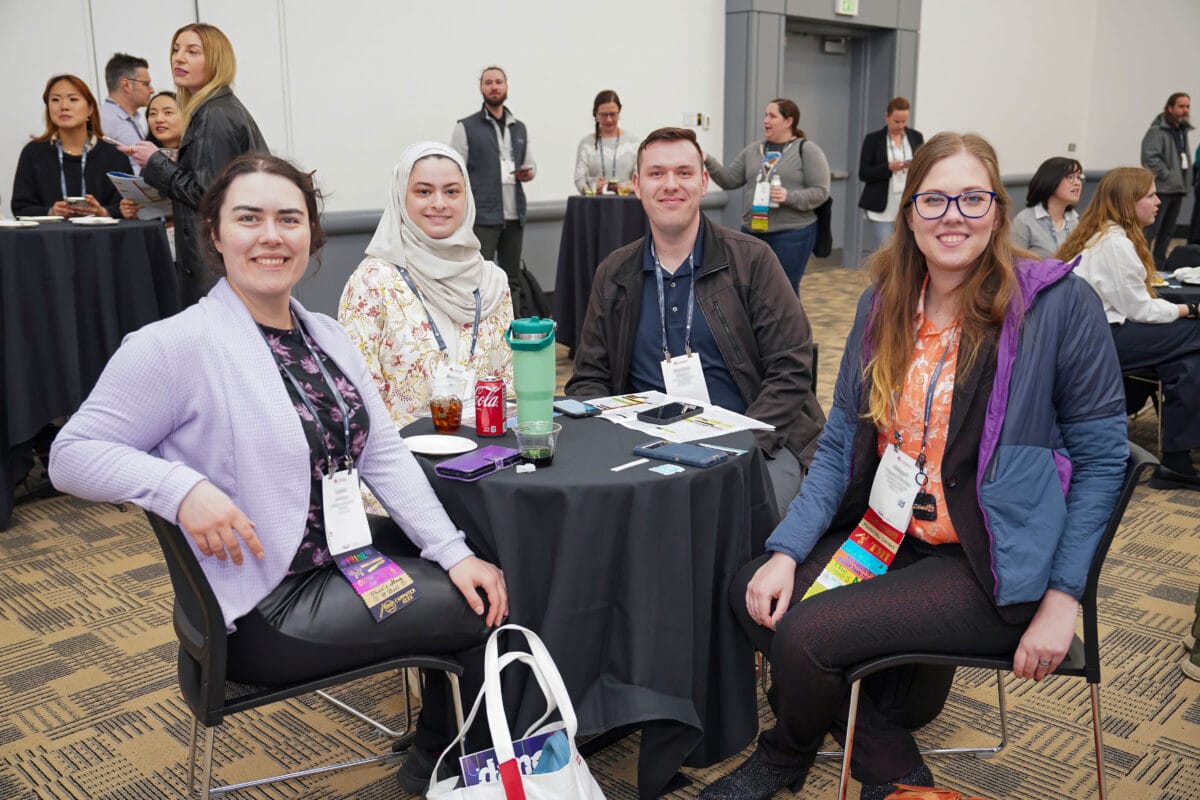 Three women engaged in discussion while seated at a table in a conference room.