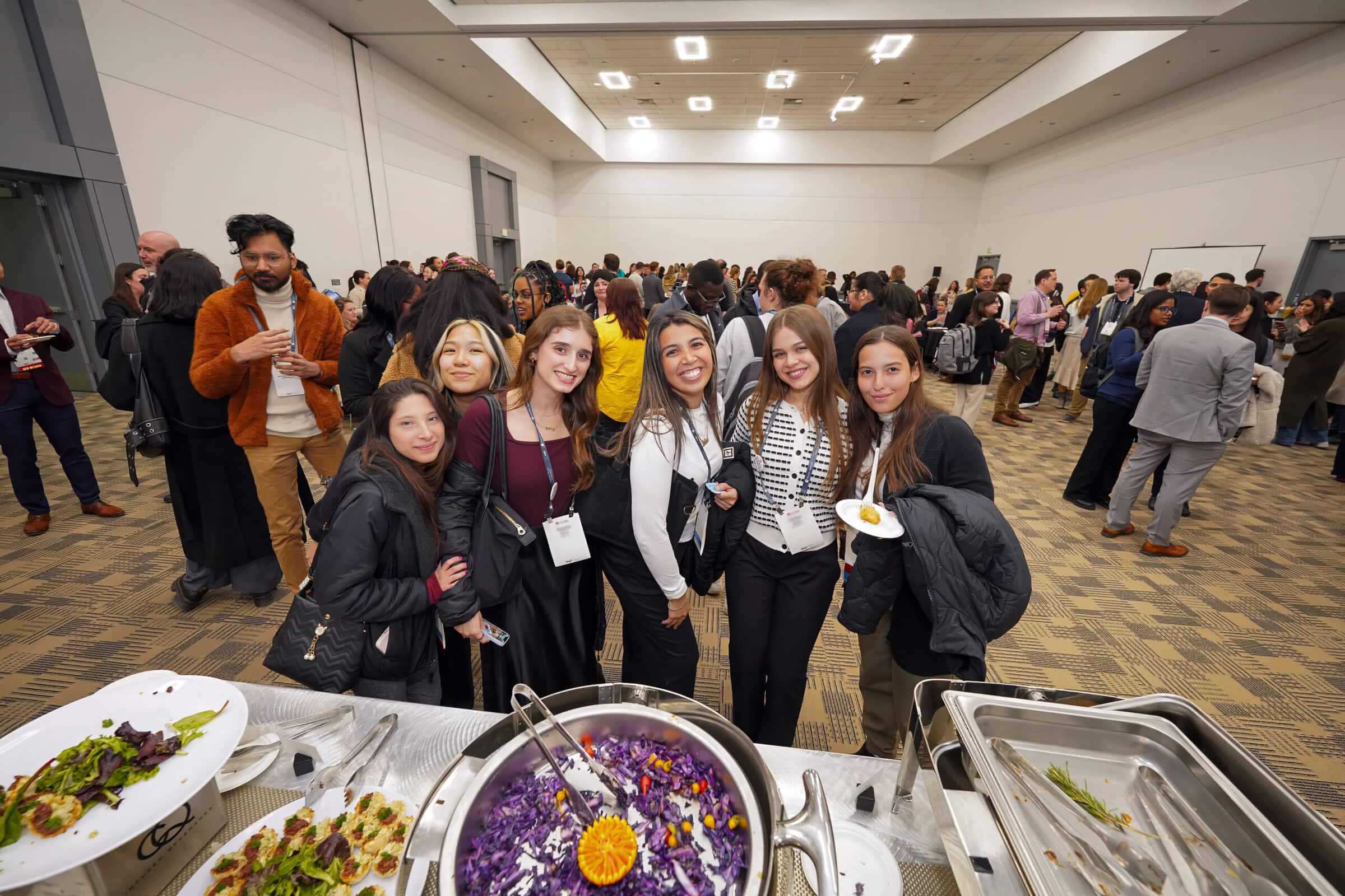 A diverse group of people stands together in front of a buffet table filled with various dishes and food options.