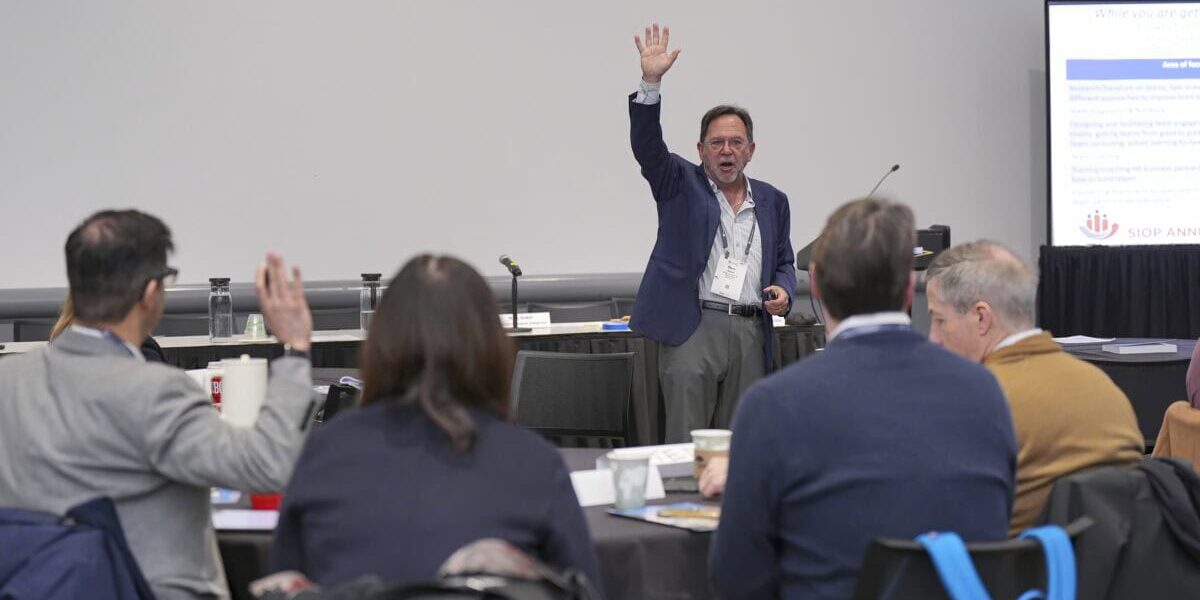 A group of Leading Edge Consortium attendees raising their hands during a session