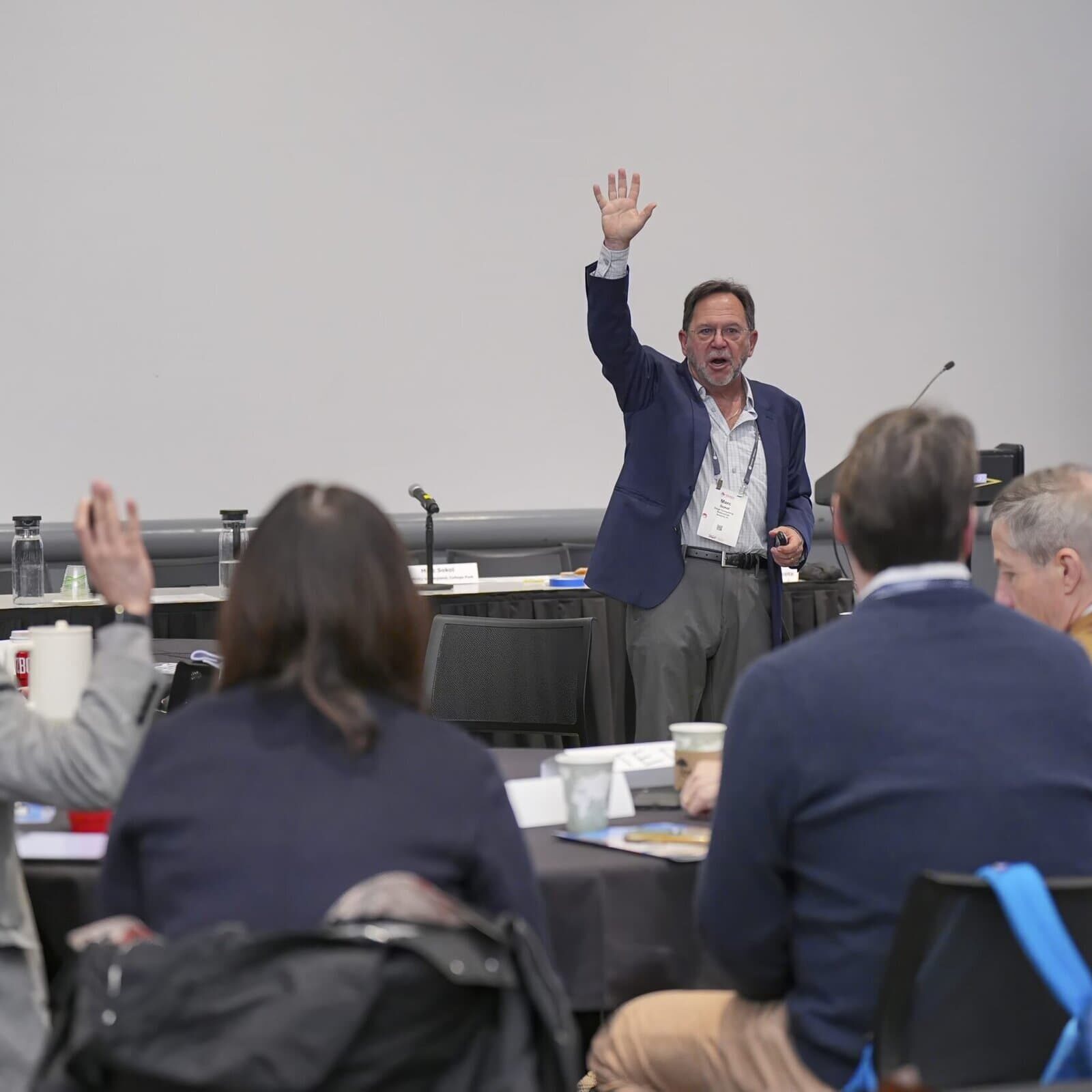 A group of Leading Edge Consortium attendees raising their hands during a session