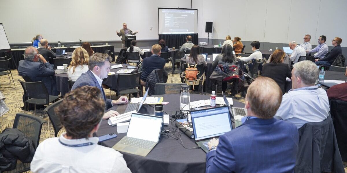 A group of people seated at tables, each using laptops, engaged in discussion and collaboration.