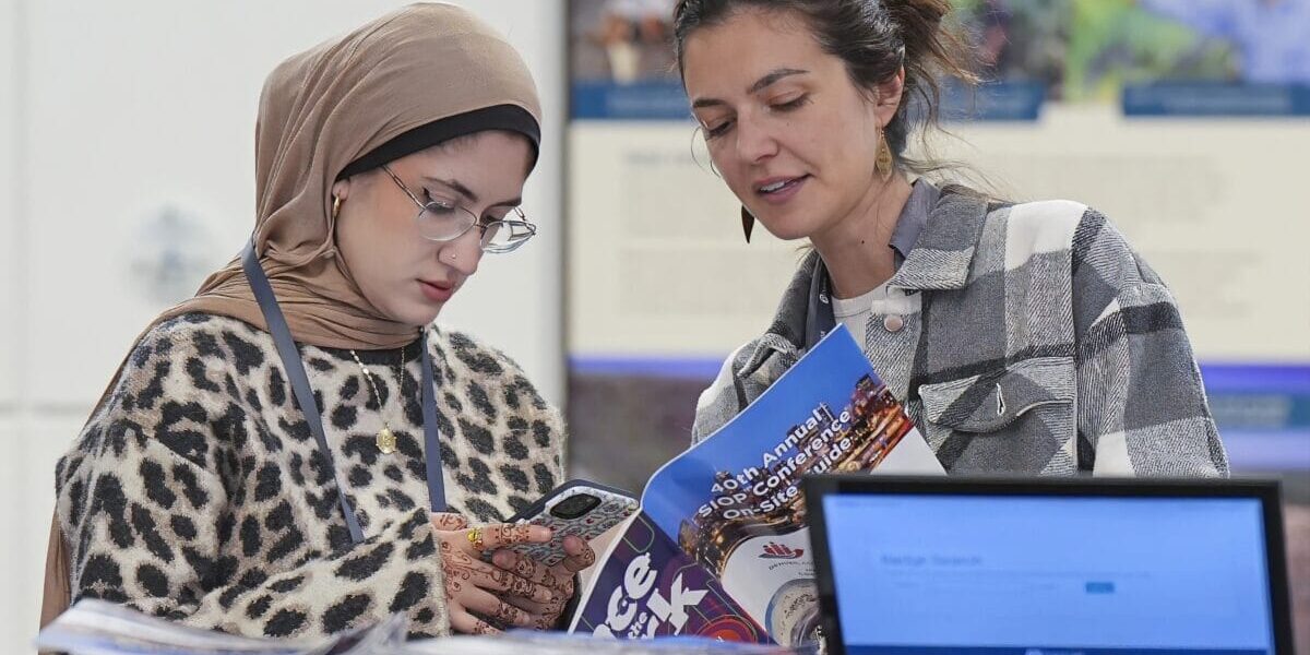 Two women are reviewing the Onsite Guide over a laptop and papers, engaged in discussion and analysis of the information presented.