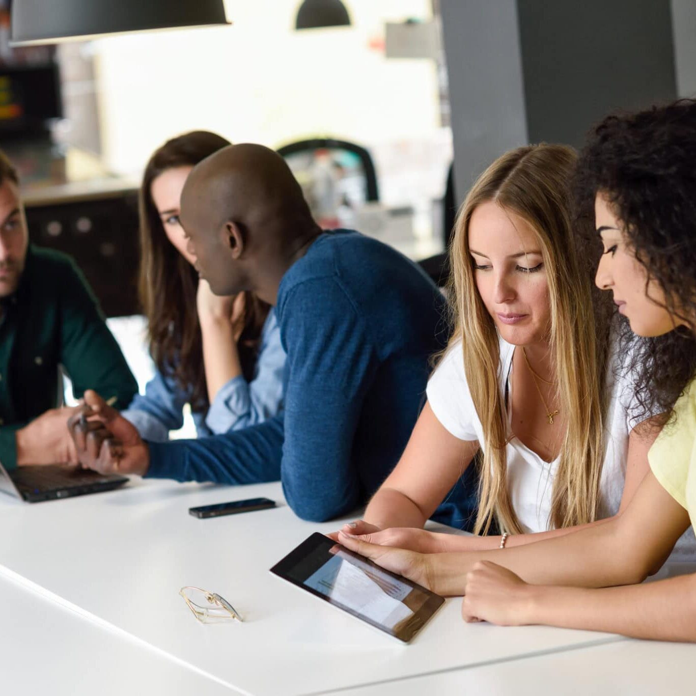 Multi-ethnic group of young people studying with laptop computer Five young people studying with tablet and laptop computer on white desk. Beautiful women and men working together wearing casual clothes. Multi-ethnic group.