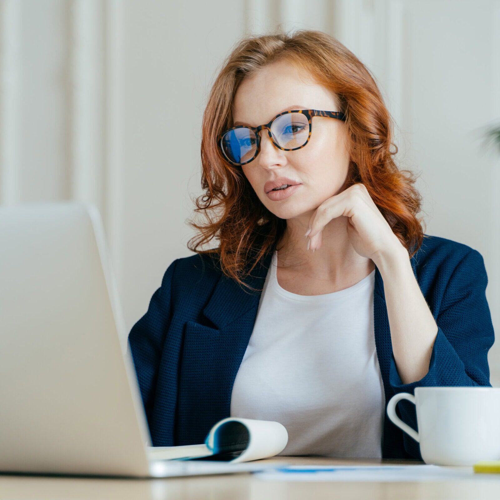 A woman in glasses sitting at a desk with a laptop