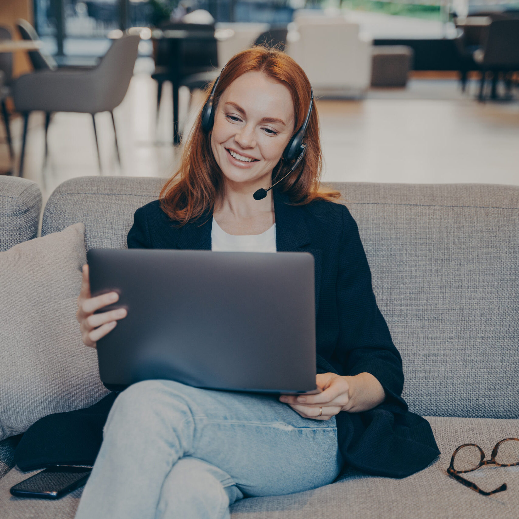 Smiling female in earphones headset and laptop watching an online webinar on the internet or enjoying e-learning