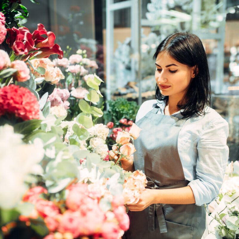 Female florist selects flowers for making a bouquet in floral shop. Floristry service, floristic business
