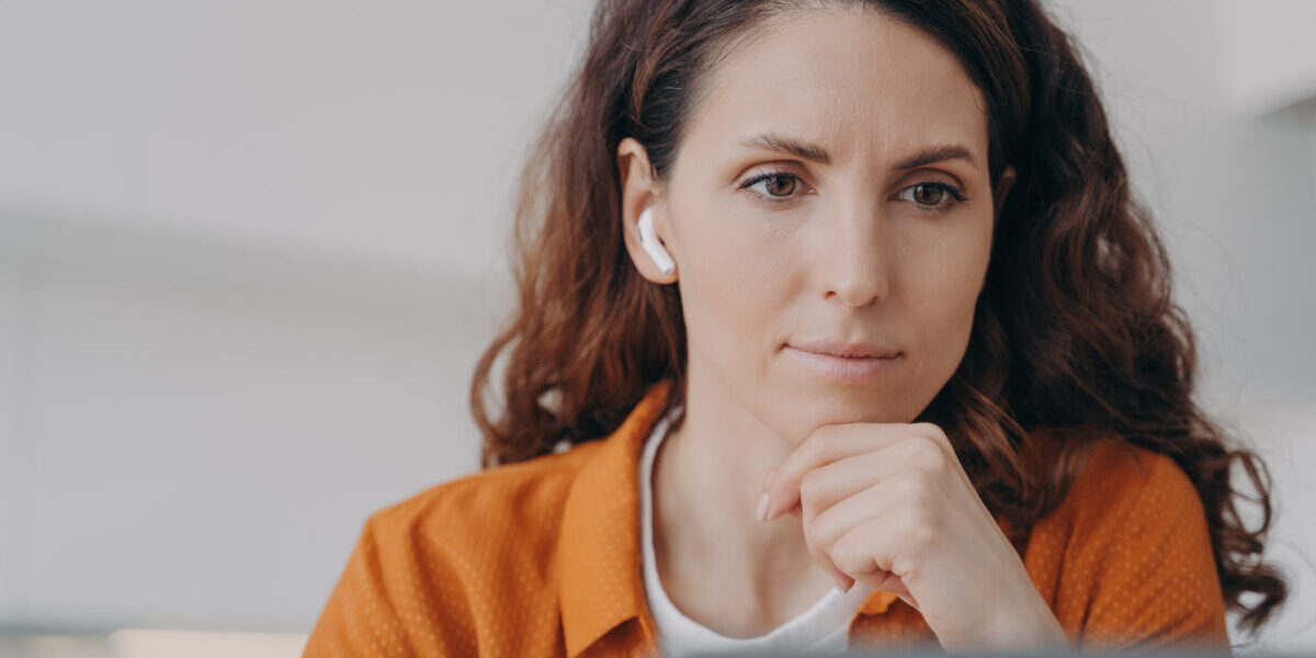 Serious focused businesswoman wearing earbud works at laptop.