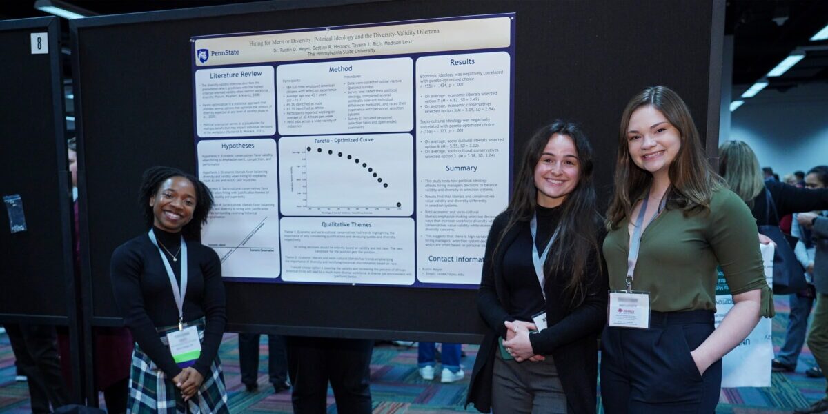 Three women standing next to a poster at a conference.