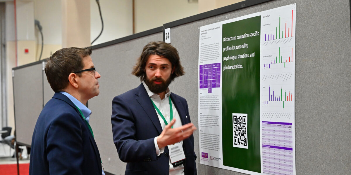 Two men talking about a poster on a wall.