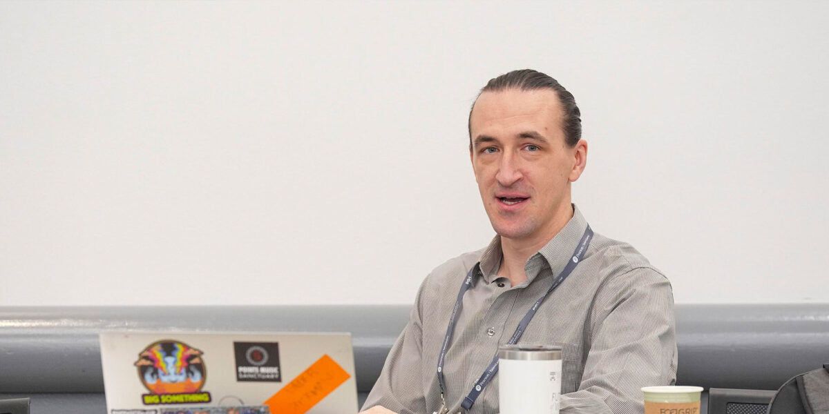 A man sitting at a table, with his laptop in front, engaging in conversation.