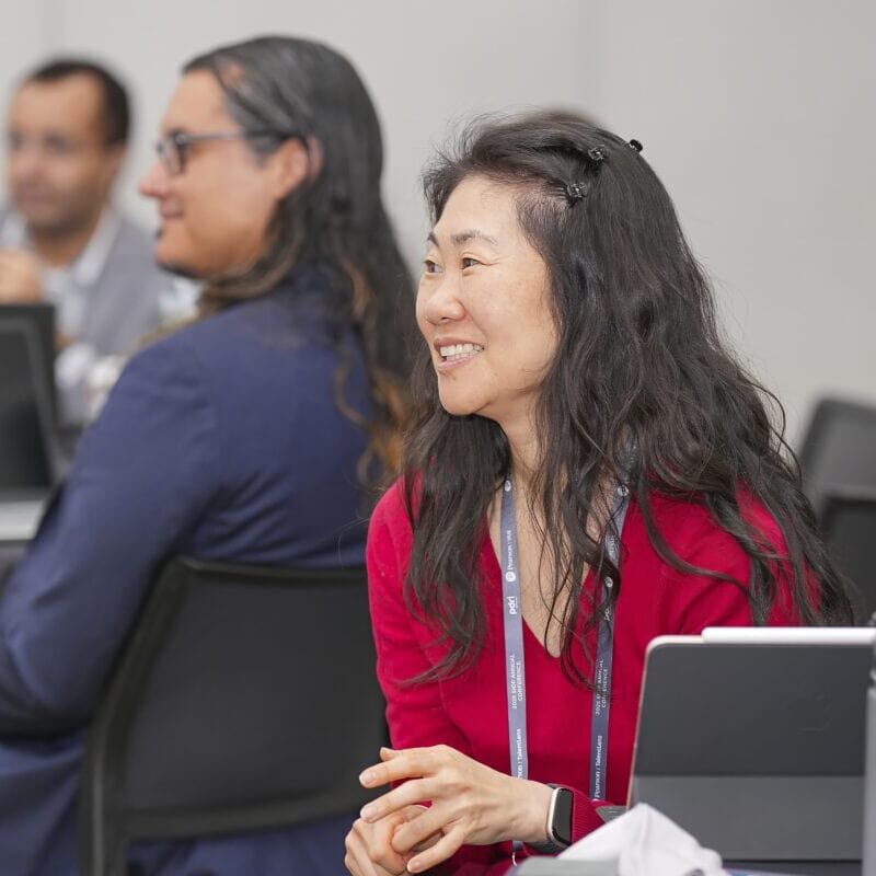 A woman sitting at a table watching presentation with a laptop