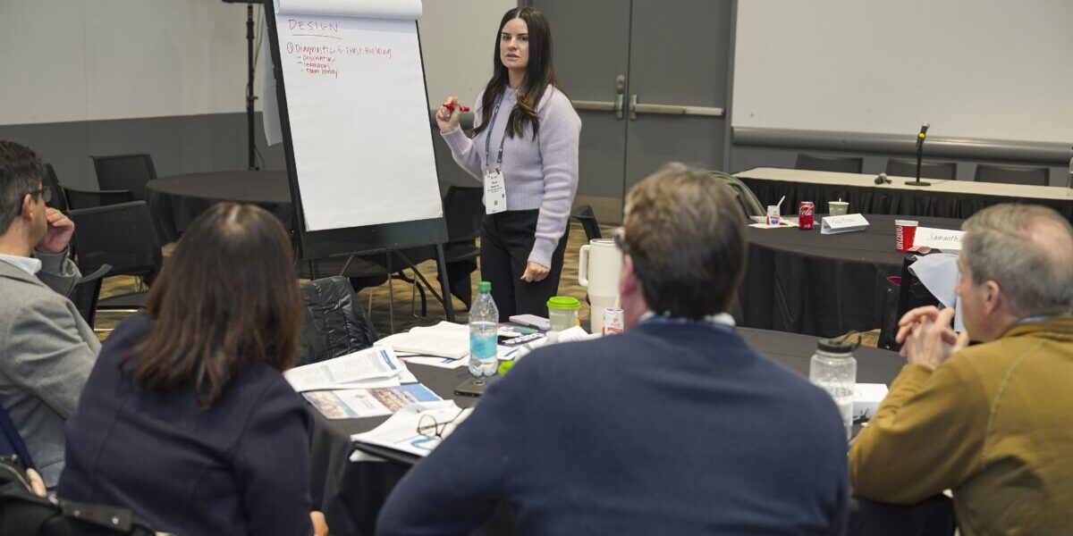 A woman stands before a group, delivering a presentation and interacting with her audience.