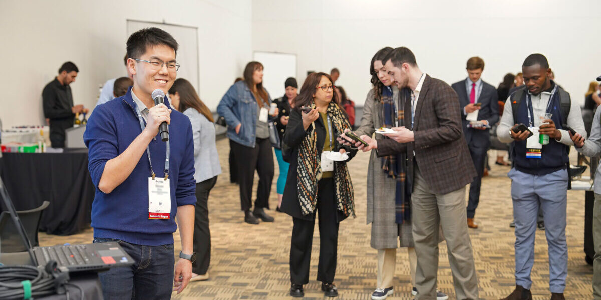 A man using a microphone to speak at an event, focused on delivering his message to the conference attendees.