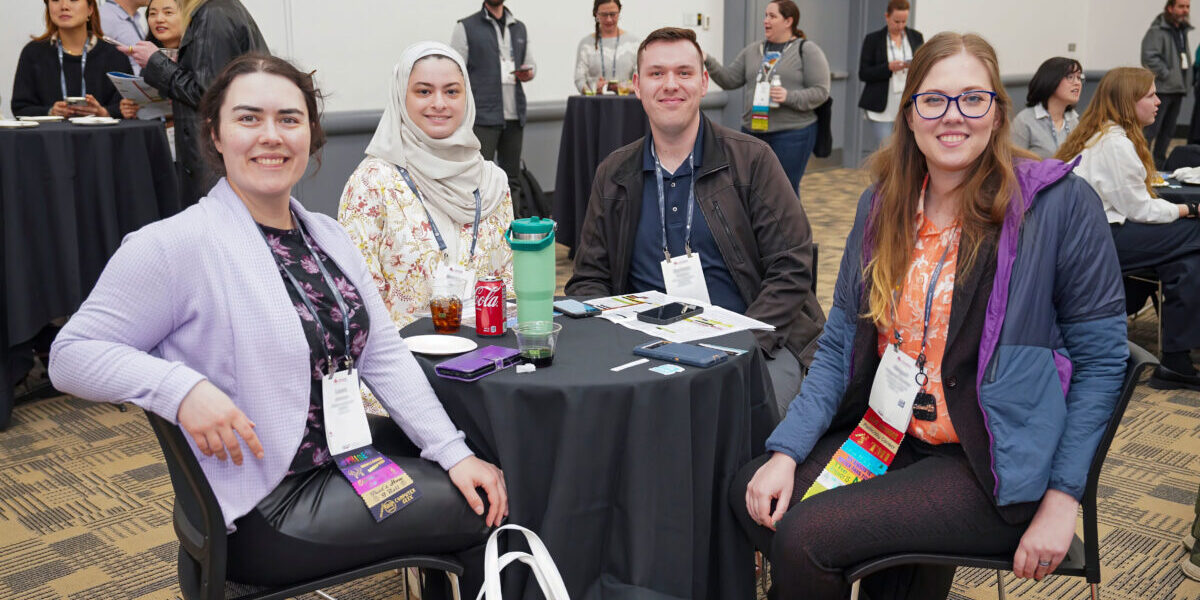 Three women engaged in discussion while seated at a table in a conference room.