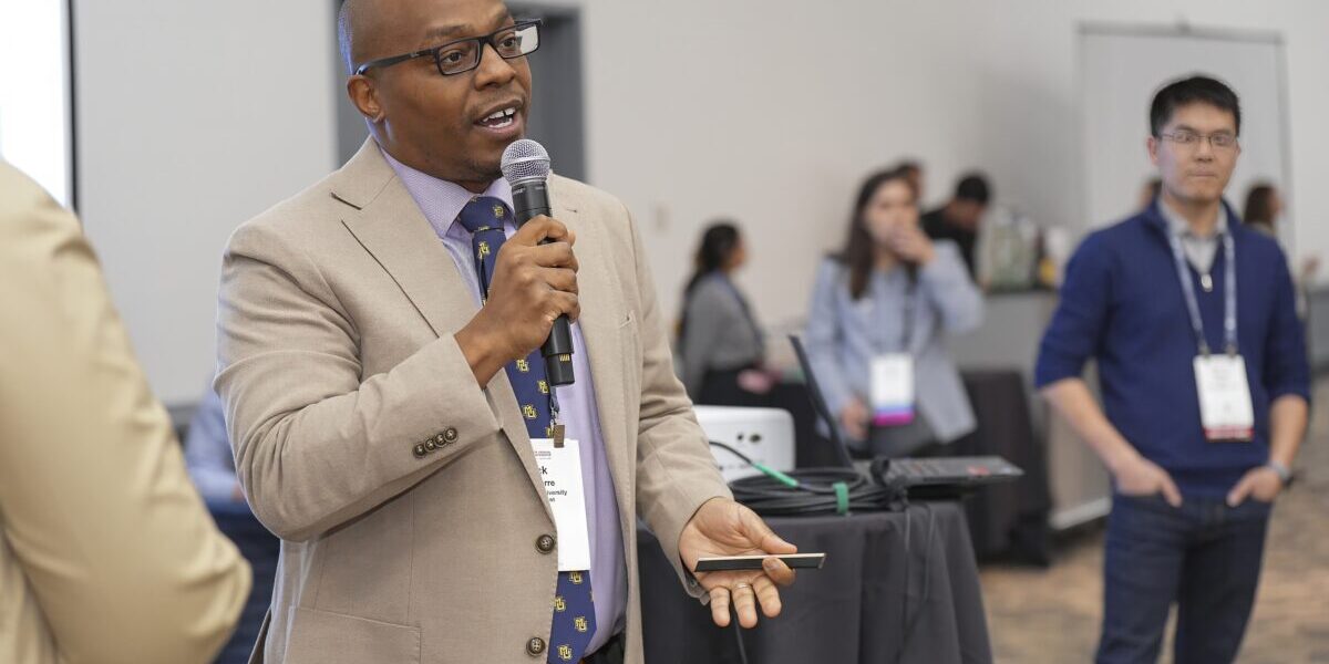 A man in a suit and tie delivers a speech into a microphone at a formal event.