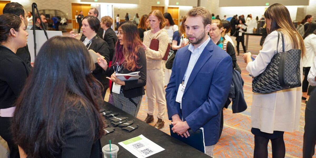 A diverse group of people gathers around a table, discussing opportunities and sharing resumes.