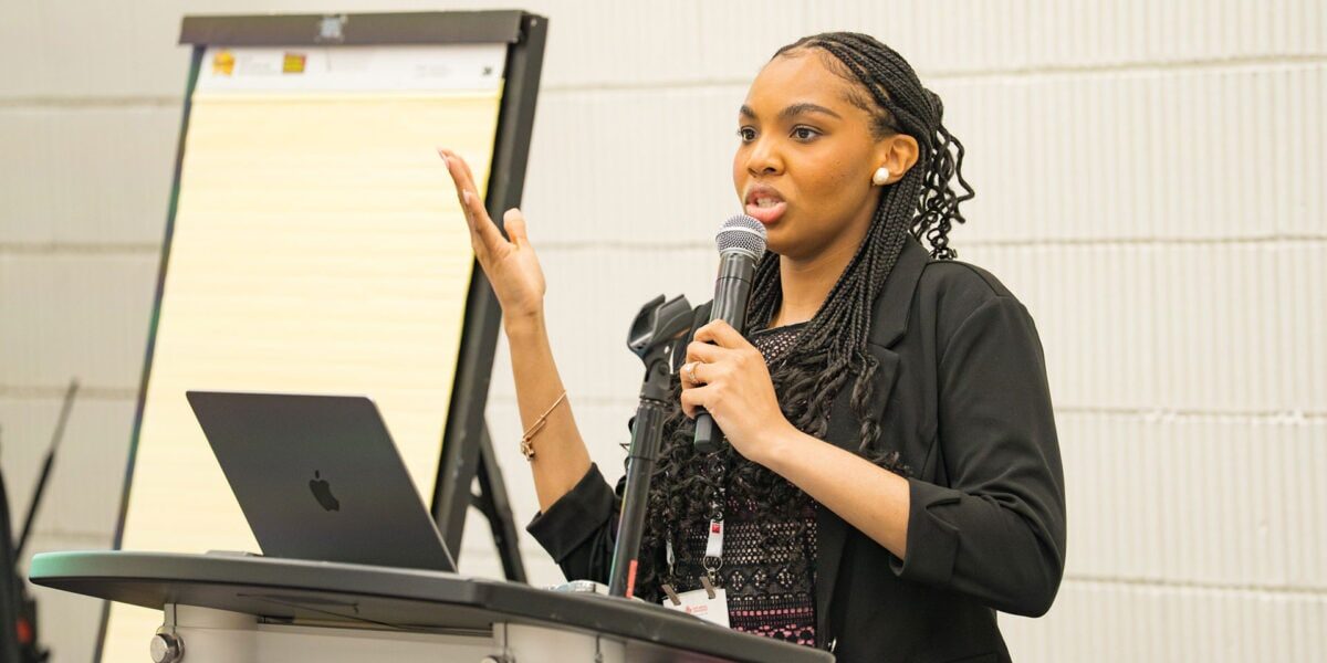 Conference speaker presenting from a podium with a microphone and laptop.