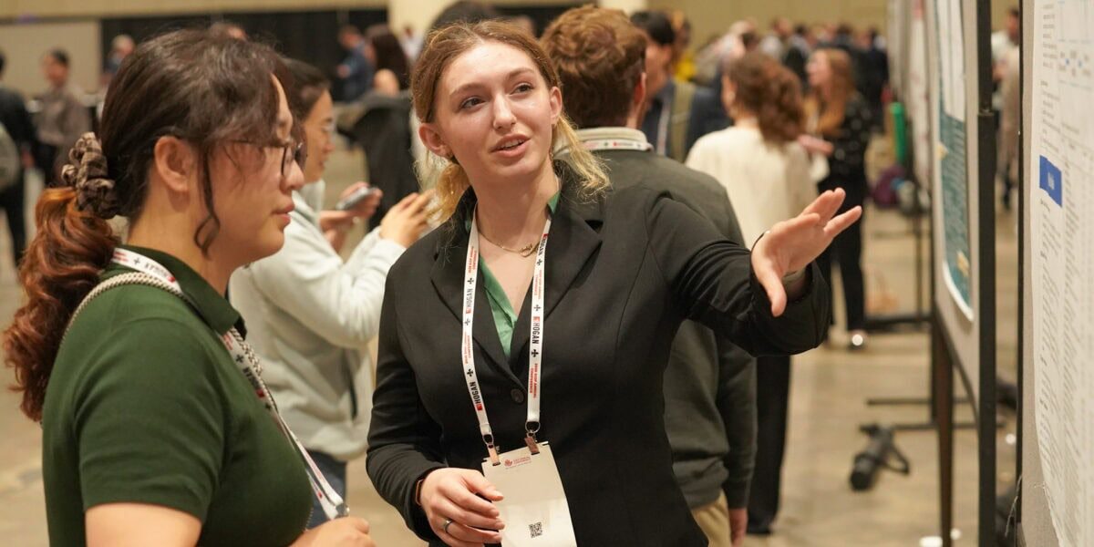 Student presenting a research poster to attendees during a conference poster session.