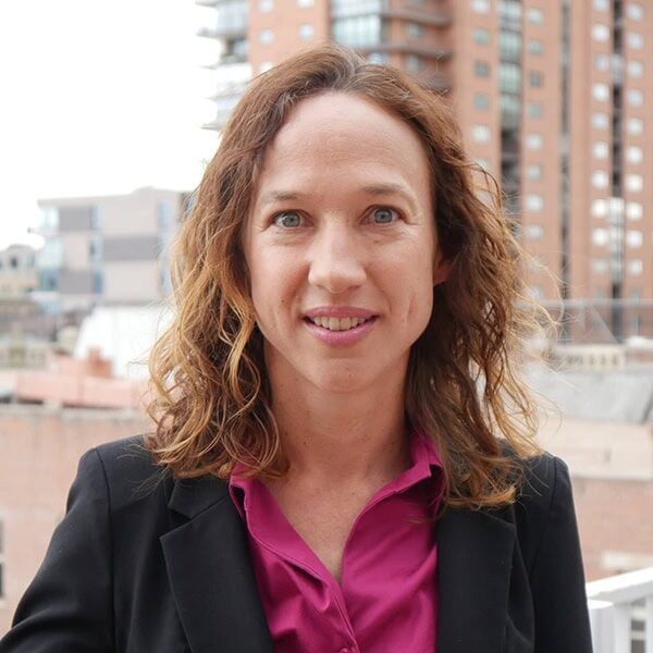 Outdoor professional headshot of Traci Sitzmann wearing a black blazer and pink shirt