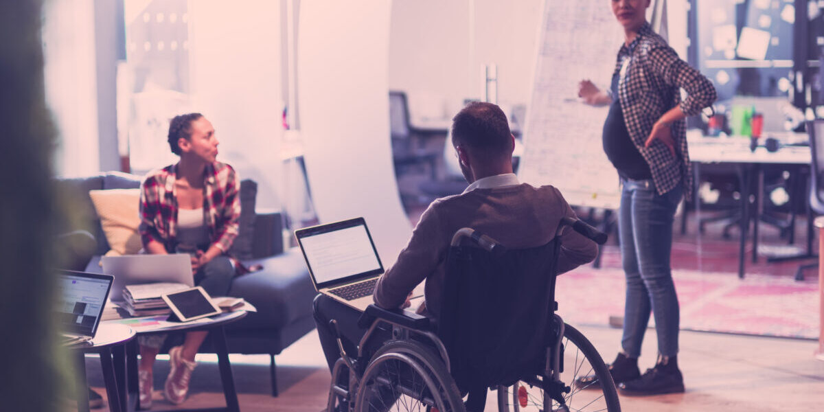 Pregnant Businesswoman Leads Creative Meeting Of Diverse Business Team In Modern Coworking Open Space Office, Disabled coworker in wheelchair attending training