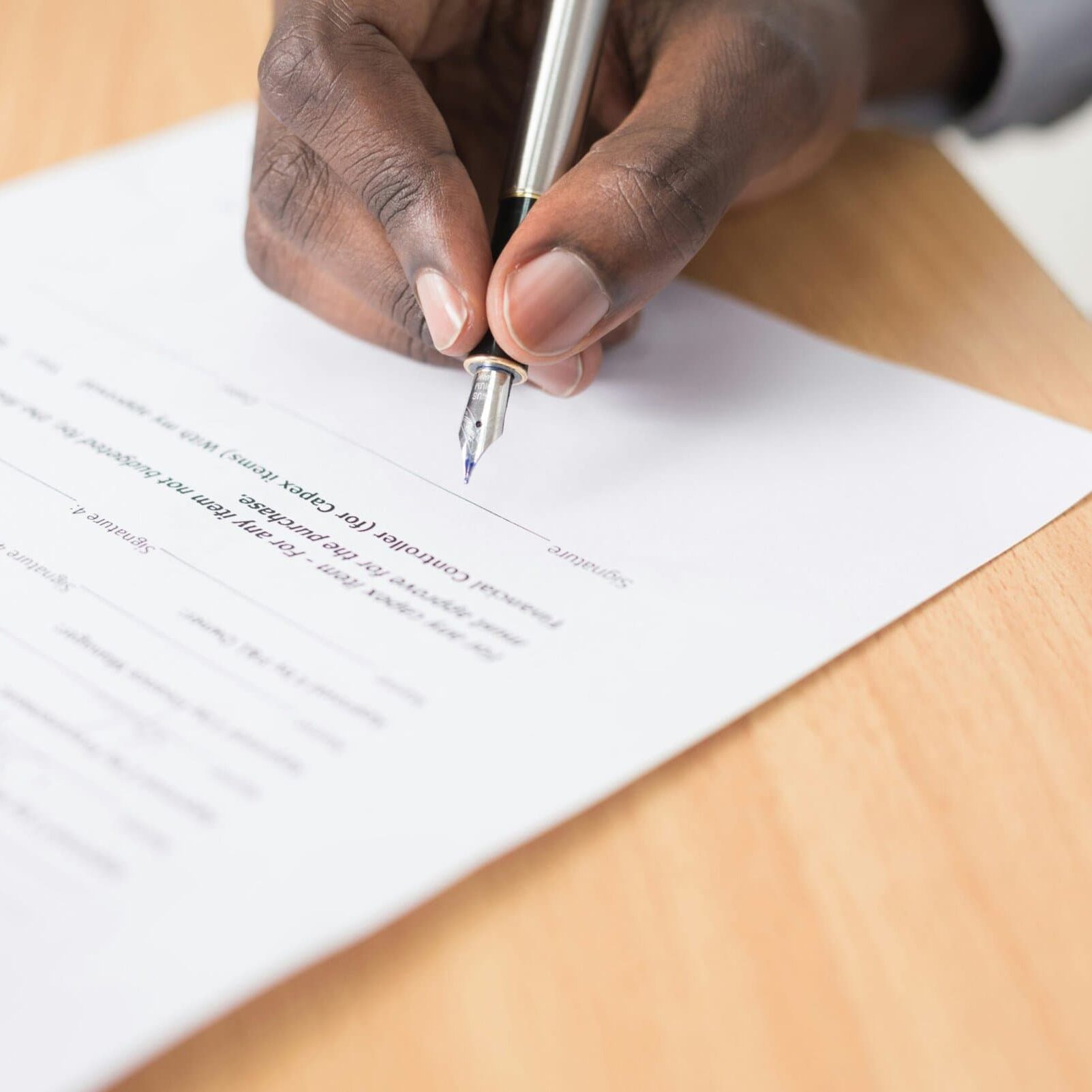 licensure a person holding a silver pen signs a piece of paper on a wood tale
