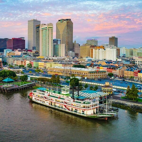 A riverboat docked in front of a vibrant city skyline under a clear blue sky.