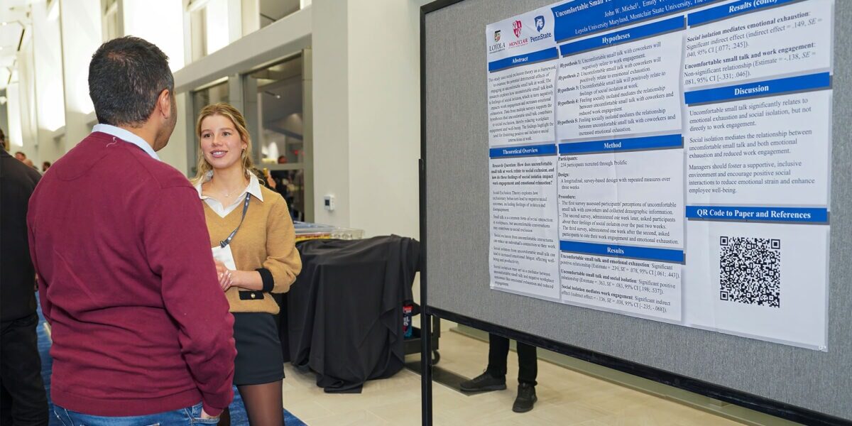 Two individuals engaged in conversation at a conference, surrounded by attendees and presentation materials.