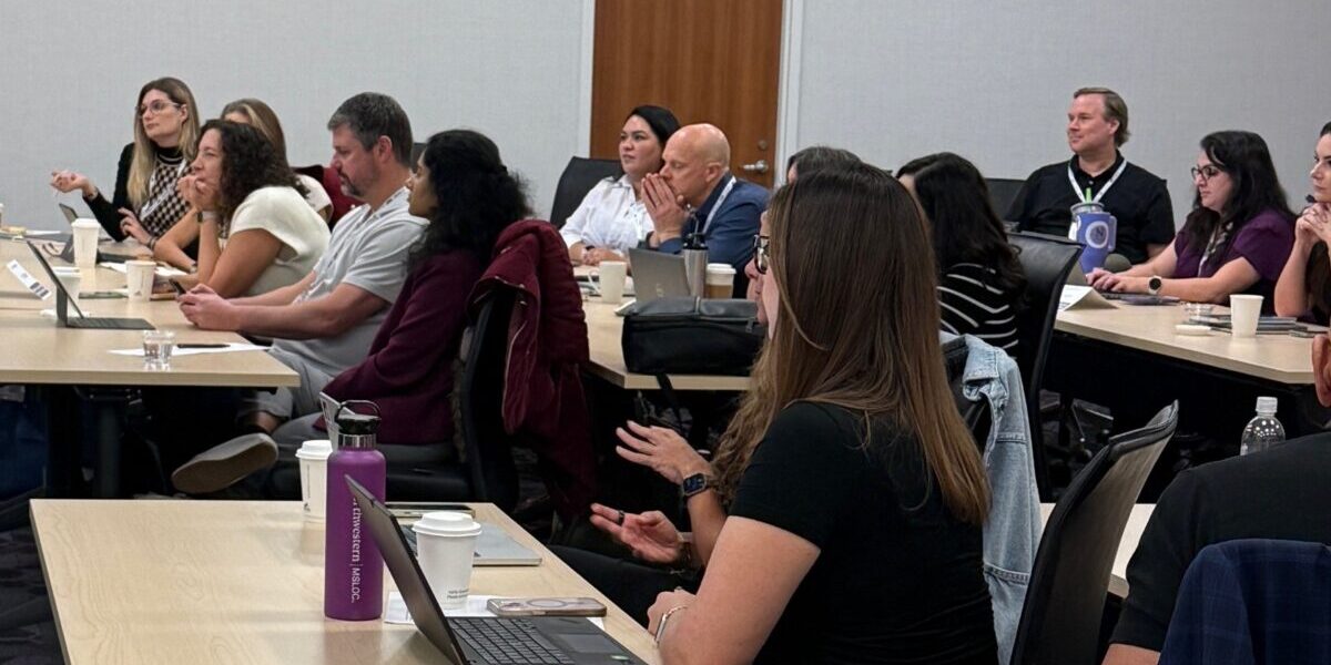 A group of people seated at tables in a conference room, engaged in discussion and collaboration.