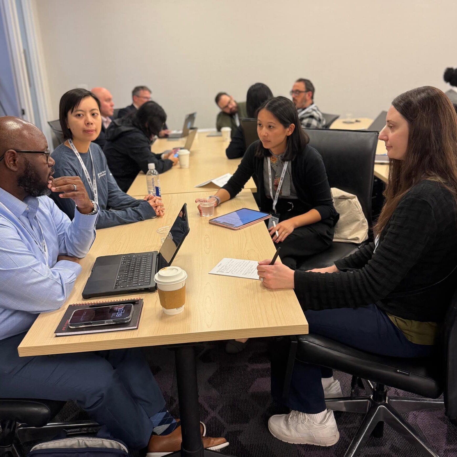 A diverse group of people collaborating around a table, each using a laptop for discussion and teamwork.