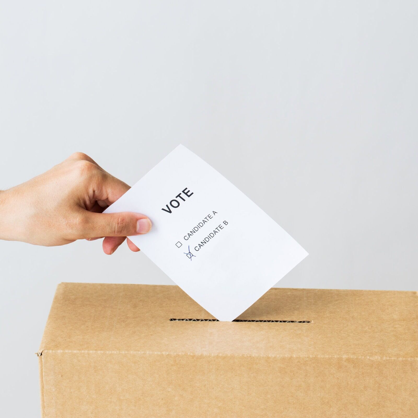 a person’s hand placing a paper ballot that has boxes to check off for candidate A or candidate B into the ballot collection box