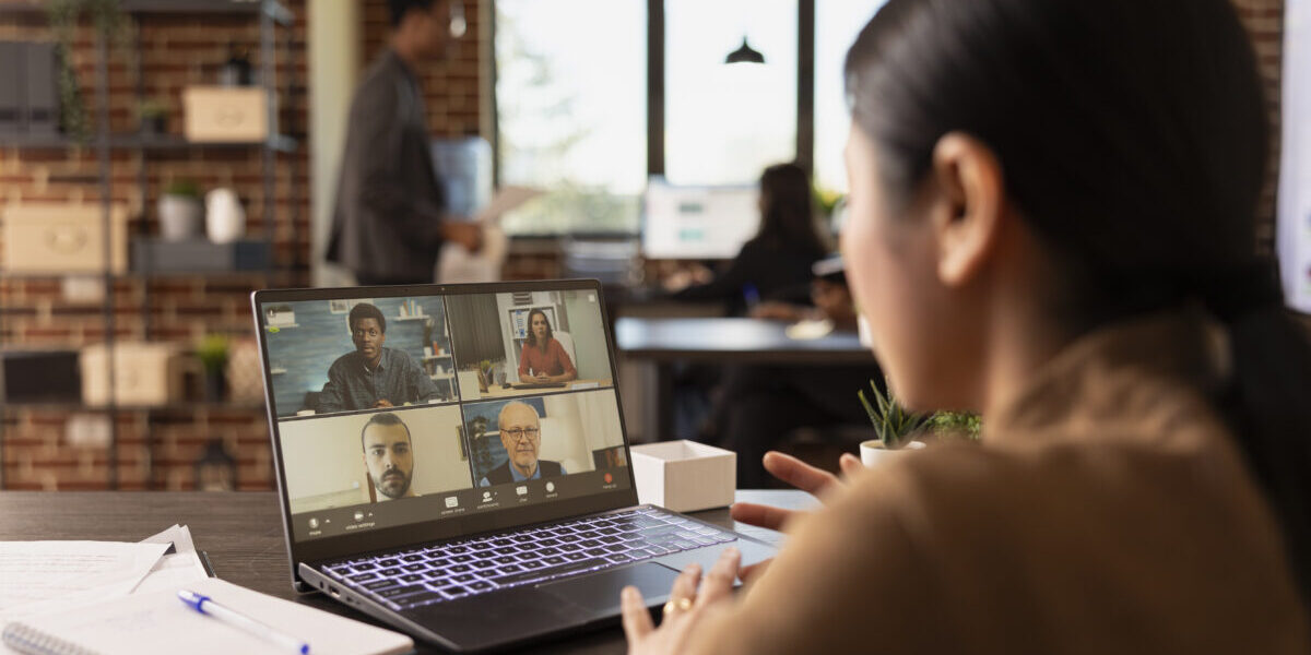 Asian businesswoman attending a virtual meeting on laptop with her remote coworkers, discussing company marketing trends. Diverse group of colleagues on a video call with female manager.